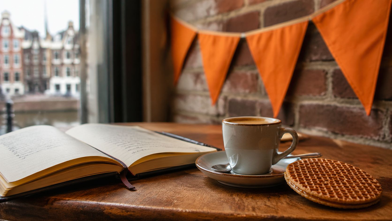 Notitieboek met handgeschreven notities op tafel naast oranje Koningsdag-decoratie en een stroopwafel